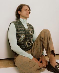 a man is sitting on the floor with his feet crossed and wearing a sweater vest