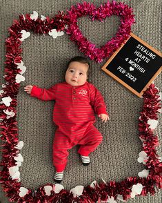 a baby is laying in a heart shaped frame with tinsel on the floor next to it