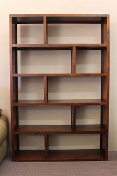 an empty bookcase in the corner of a room with a chair and ottoman behind it