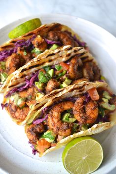 shrimp tacos with cabbage, avocado and cilantro on a white plate