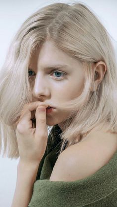 a woman with blonde hair and blue eyes posing for the camera, wearing a green top