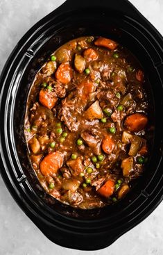 a crock pot filled with stew and carrots on top of a white table