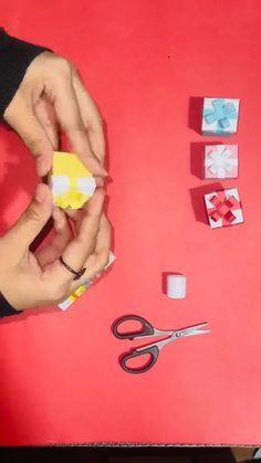 someone is cutting out small pieces of paper with scissors and glue on a red surface