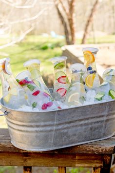 a metal bucket filled with ice and lemon slices on top of a wooden table next to a tree