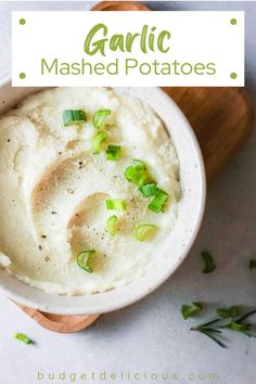 a white bowl filled with mashed potatoes on top of a wooden cutting board next to green onions