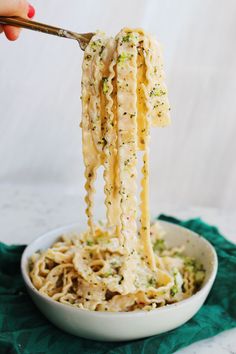 someone is lifting noodles from a bowl with broccoli