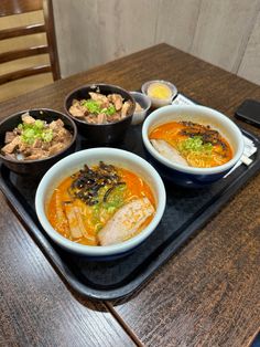 three bowls of soup on a tray with chopsticks