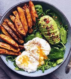 a plate with eggs, avocado and spinach on it next to a fork