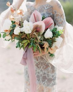 a woman holding a bouquet of flowers in her hand and wearing a dress with sheer sleeves