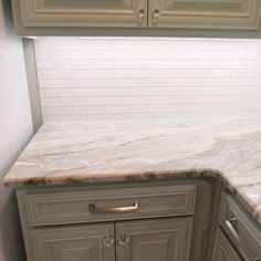 a kitchen with marble counter tops and gray cabinets in the corner, along with white subway backsplash