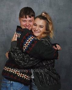 two people hugging each other in front of a gray background