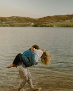 two people are walking in the water with their arms around each other and one is carrying another person