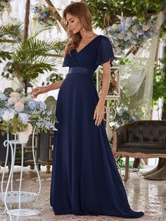 a woman in a long blue dress standing next to a chair and flowers on the floor