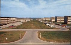 an empty parking lot with cars parked on the other side and buildings in the background