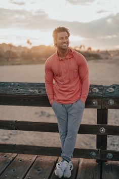 a man sitting on top of a wooden bench next to the ocean in front of a sunset