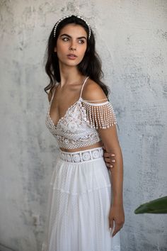 a woman wearing a white dress and headpiece standing in front of a concrete wall