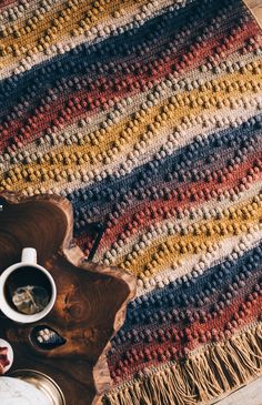 a crocheted blanket and cup of coffee on a wooden table with other items