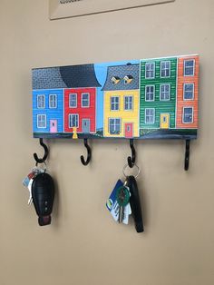 three hooks are hanging on the wall with houses painted on them and keys attached to them