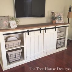 a tv mounted on top of a white entertainment center with baskets under it and a flat screen television above