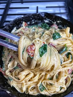 a skillet filled with pasta and spinach on top of a stove burner