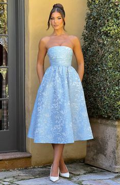 a woman standing in front of a door wearing a blue strapless dress with flowers on it