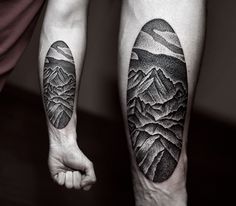 two people with tattoos on their legs standing next to each other in front of mountains