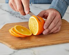 a person cutting up an orange on top of a wooden cutting board with a knife