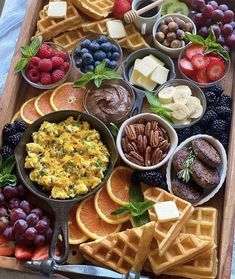 a wooden tray topped with waffles, fruit and other foods