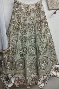 Sequins Embroidered Indian Bridalwear of white sheer choli blouse with taffeta silk lining and feather trim. Intricately embroidered white long trailed skirt lengha with 3D floral cutout embellished on the hemline. Flower patterns are embroidered in ascending order from the waist belt of the lengha flowing towards the long trail. Each flower pattern is accented with feathers in the center. #indianbridalwear2021 #latestlehengacholi #3Dembroideredlehenga #champagnebridallengha #sequins&featherwork Elegant Embellished Net Sharara, Embroidered Fabric With Sequins For Wedding, Party-ready Silver Sharara With Intricate Embroidery, Party Silver Sharara With Intricate Embroidery, Elegant Sequined Lehenga For Festivals, Traditional Georgette Gown With Sequins, Party Wear Embroidered Fabric With Pallu For Wedding, Traditional Embellished Net Gown, Embroidered Net Dress For Reception