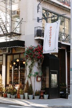 an outside view of a building with flowers and plants on the sidewalk in front of it