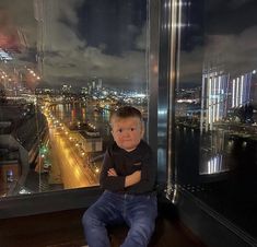 a little boy sitting on top of a window sill looking out at the city