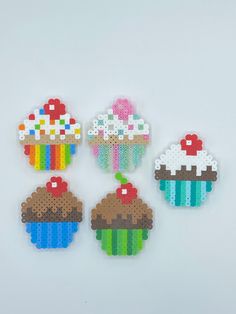 four cupcakes made out of perler beads on a white surface, each with different colors