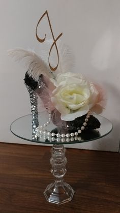 a glass table topped with a white rose and black shoe cake topper next to a wall