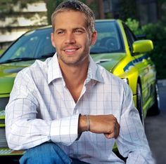 a man sitting on the ground next to a green car and smiling at the camera