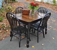 a wooden table with four black chairs and a basket on top of it in front of some flowers