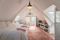 an attic bedroom with white bedding and pink rugs on the floor in front of it