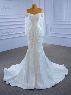 a white wedding dress with beading on the shoulders and off the shoulder, is displayed in front of a mannequin