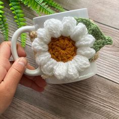 a hand holding a coffee cup with a crocheted flower on it's side