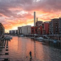 a man riding a paddle board on top of a river next to tall buildings at sunset