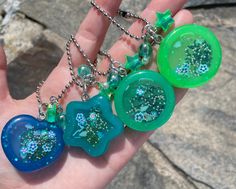 a hand holding four different colored necklaces in it's palm, with blue and green designs on them