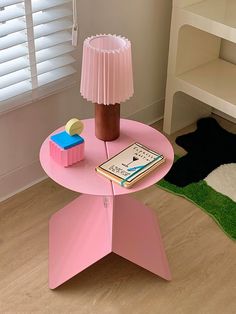 a pink table with a lamp on top and a book sitting on it's side