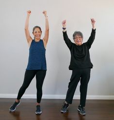 two older women are doing yoga in front of a wall with their arms raised up