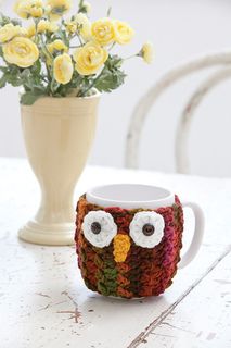 a crocheted owl coffee cup holder next to a vase with flowers