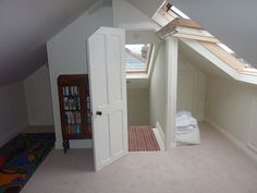 an attic bedroom with slanted roof and white walls, carpet flooring and bookcases