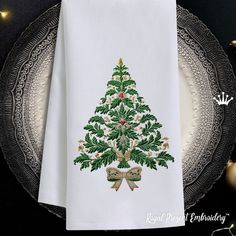 a white napkin with a christmas tree on it and bows around the edges, sitting on a plate