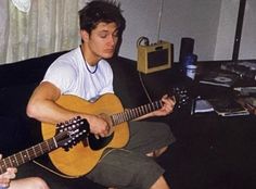 a man sitting on top of a couch holding a guitar next to another person playing the guitar