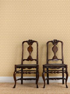 two wooden chairs sitting next to each other in front of a wall with polka dots