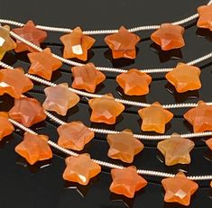 an orange necklace with star shaped beads on a black surface and silver chains around it