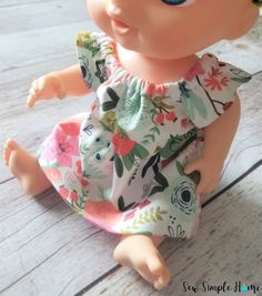 a baby doll sitting on top of a wooden floor wearing a flowered dress and hat