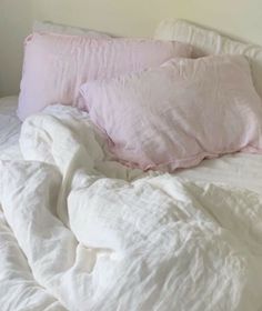 an unmade bed with white sheets and pink pillows